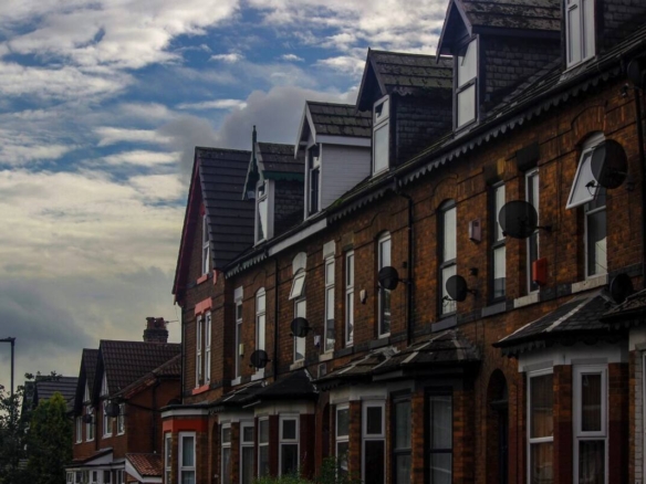 Row of red brick terraced houses in a UK suburb under a cloudy sky