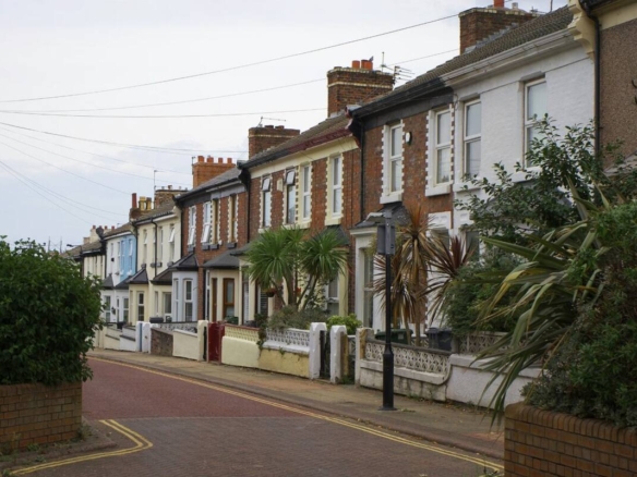 Quiet UK residential street lined with brick terraced houses and front gardens